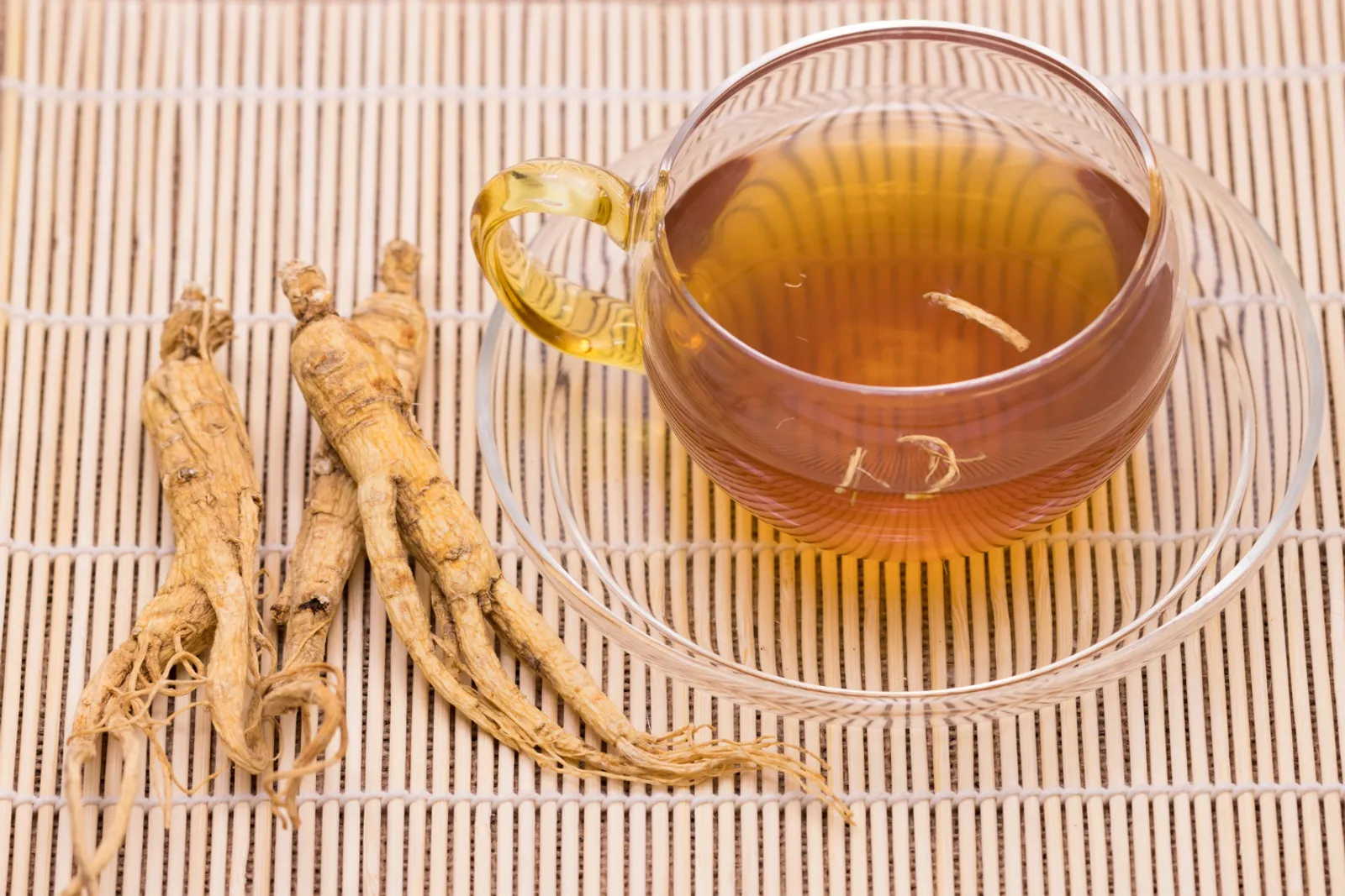Des racines séchées de ginseng sibérien, une théière en verre et un mortier sur une table de cuisine éclairée par la lumière naturelle.