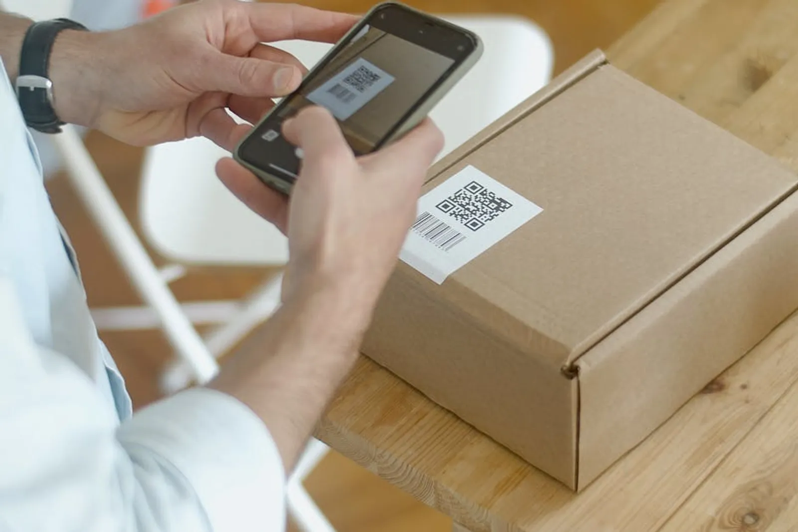 Un technicien scanne un QR code sur un produit dans un atelier, avec un tableau de contrôle en arrière-plan.