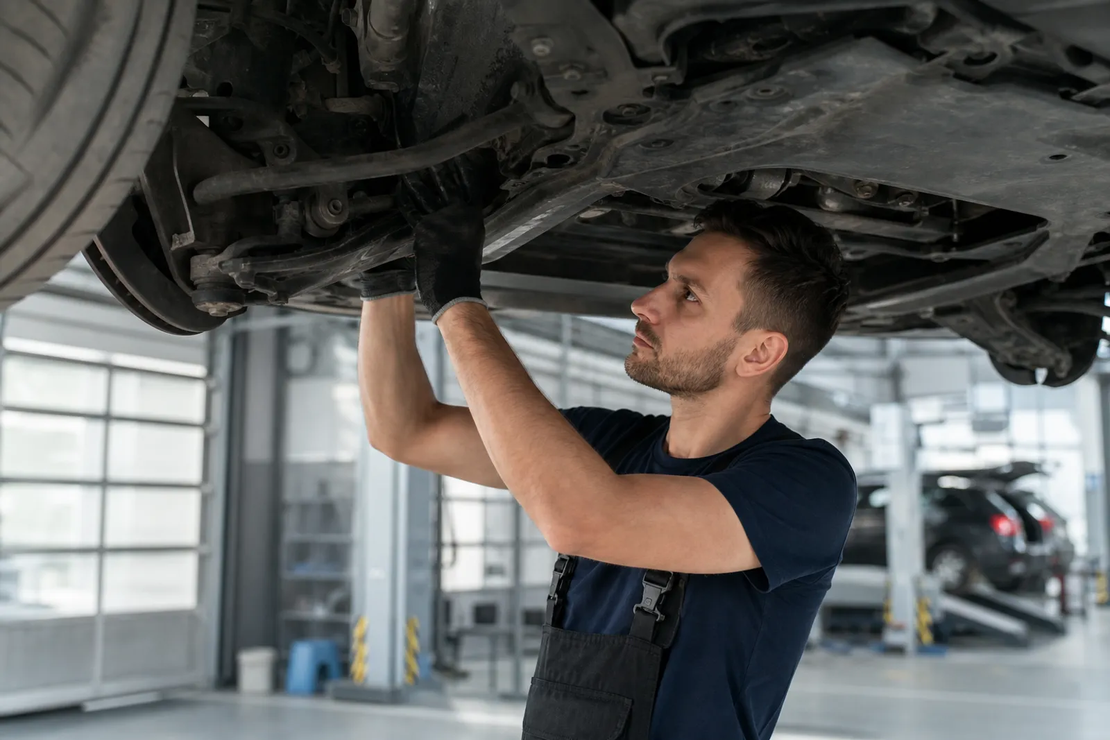 Un technicien examine le dessous d'une voiture sur un pont élévateur dans un centre de contrôle technique.