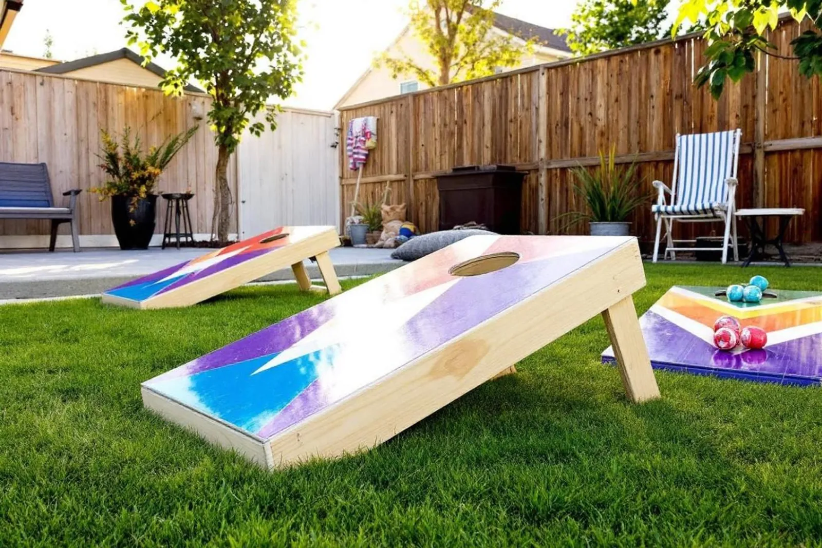 Des amis et une famille jouent au cornhole dans un jardin ensoleillé, autour de planches en bois posées sur la pelouse.