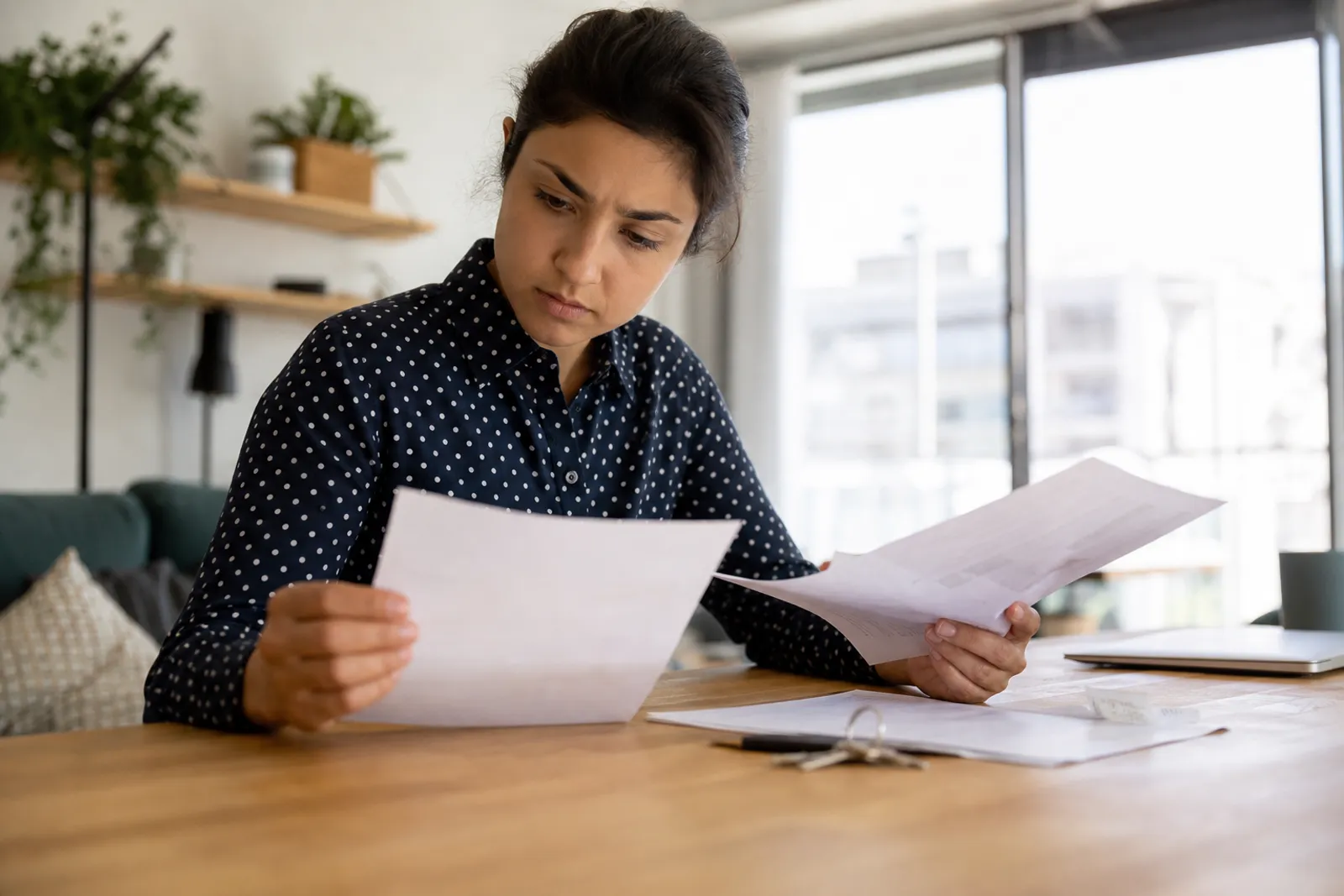 Locataire consultant des documents de bail et un relevé bancaire à une table, clés d'appartement posées à côté.