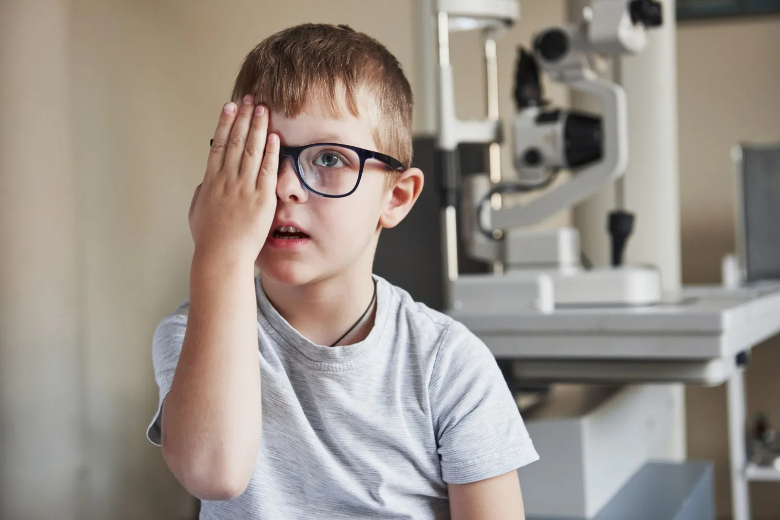 Un enfant passe un examen de vue chez l’ophtalmologiste, accompagné d’un parent, dans un cabinet lumineux.