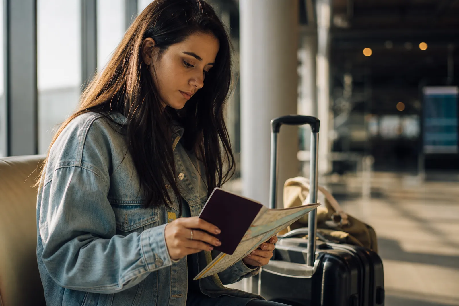 Voyageur consultant son passeport et une carte touristique à l'aéroport, valise posée à ses pieds.