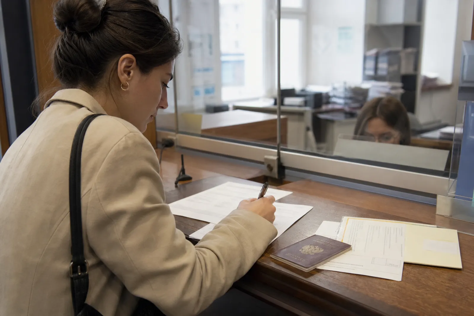 Une personne remplit un formulaire administratif à un guichet de mairie pour refaire sa carte d'identité.