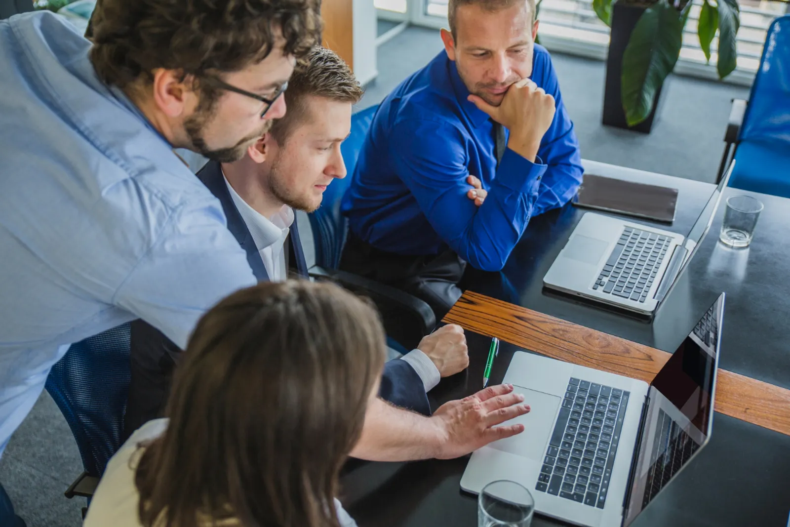 Une équipe de bureau collabore autour d’un écran de visioconférence et d’ordinateurs portables dans un environnement professionnel lumineux.