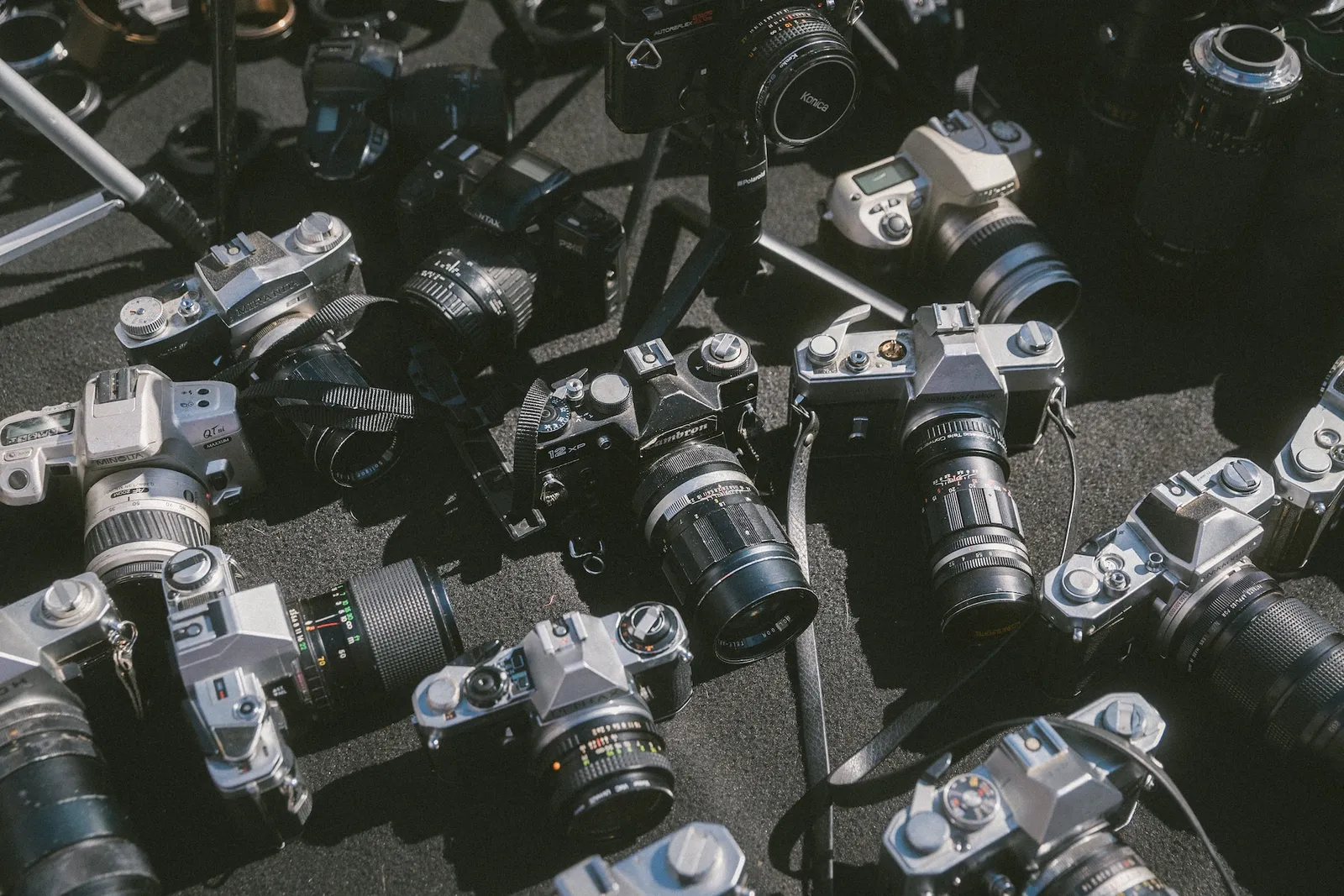 Un appareil photo argentique des années 70 en cours de restauration sur un établi, avec des outils de précision et des mains qui nettoient l’objectif.